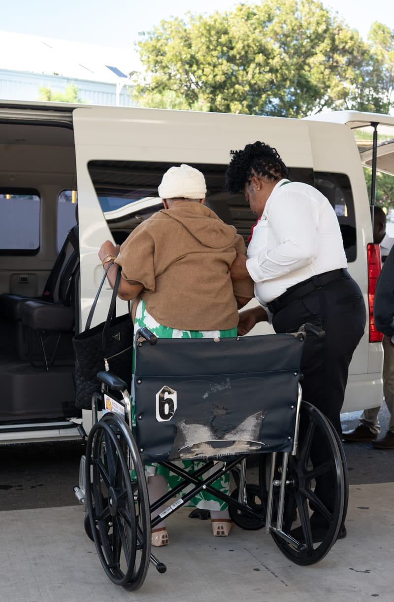 Staff helping elderly passenger board a van — our values in action